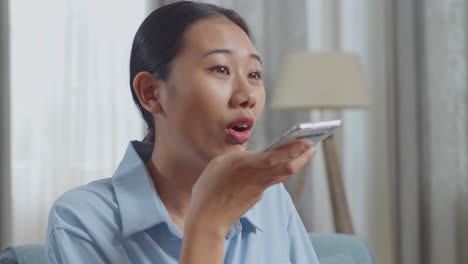 close up of asian woman recording voice message on smartphone while sitting on sofa in the living room