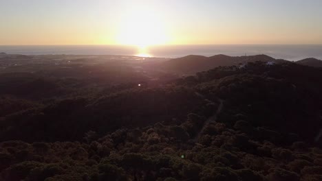 Spectacular-large-white-sun-with-yellow-halo-setting-on-ocean-horizon-at-sunset-by-lookout-tower,-pull-back-aerial