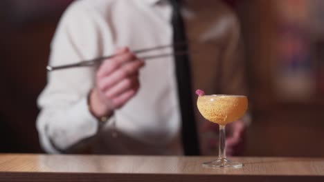 primer plano de cóctel alcohólico y fondo borroso de un barman decorándolo