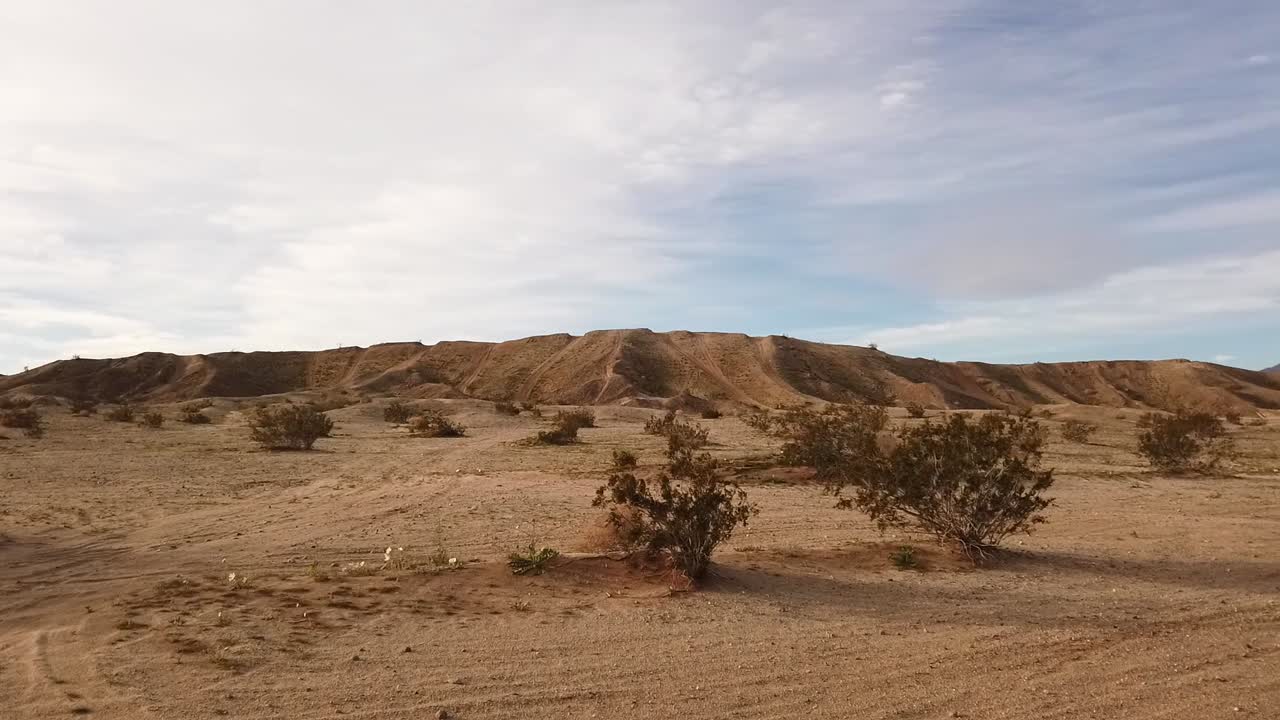 오프로드 차량 타이어 트랙과 그 너머로 솟아오르는 언덕으로 표시된 모래 표면의 패닝 뷰