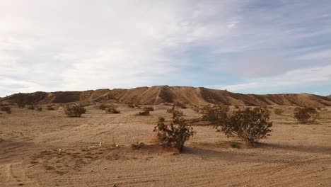 Panning-view-of-sandy-surface-marked-with-off-road-vehicle-tire-tracks-and-rising-hills-beyond