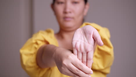 A-close-up-of-a-woman-wearing-a-yellow-dress-is-stretching-her-left-arm-while-pinching-and-massaging-herself-from-her-wrist-down-to-her-fingers