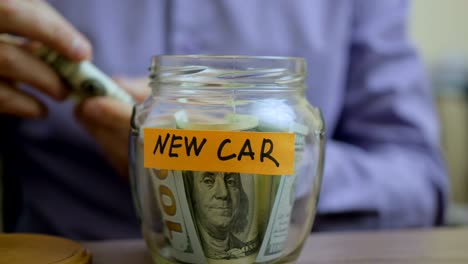 hombre caucásico poniendo un frasco de vidrio puesto en una mesa de cajón con sus ahorros para el futuro coche nuevo
