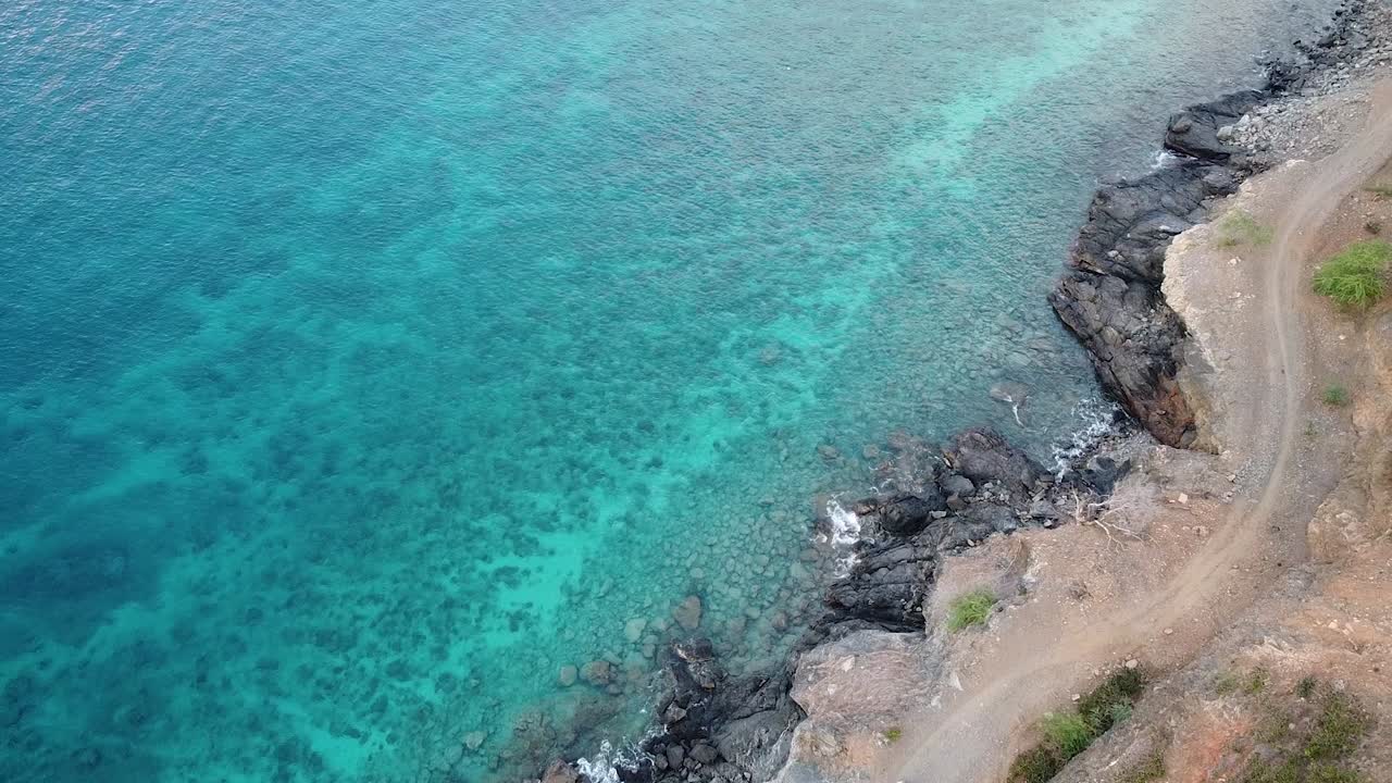 Aerial birds eye view of white car driving on coastal track next to turquoise ocean water in Timor-Leste, Southeast Asia