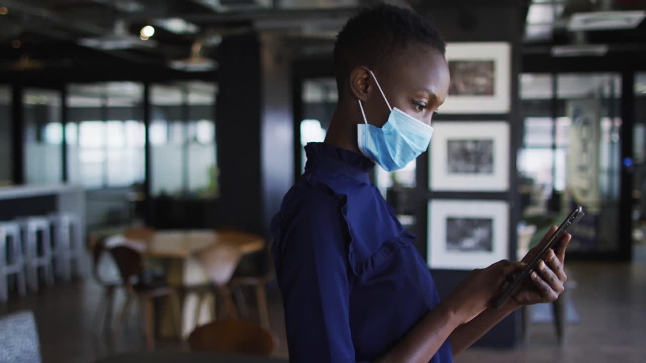 Portrait of african american woman wearing face mask using digital tablet at modern office