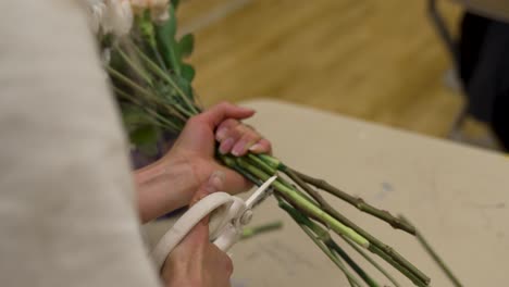 un florista corta los tallos de las flores en un ramo antes de unirlos