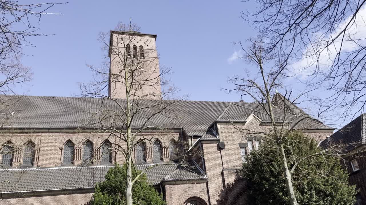 old big brick church with big clock on the tower behind old trees