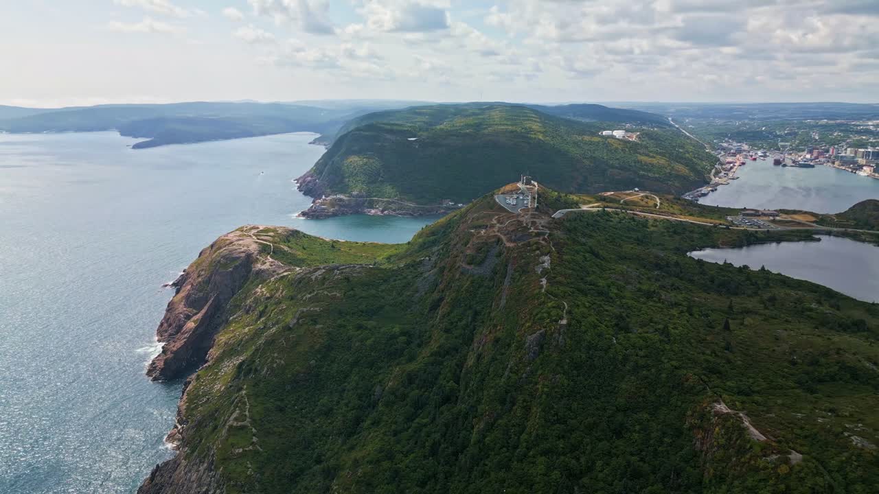 A drone follows the narrow, winding ridge of Signal Hill as it slopes toward the ocean, revealing green grass, cliffs, and glimpses of the coast under cloudy skies
