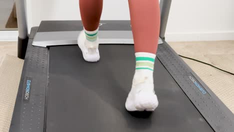 a woman walks on a treadmill in a well-lit home gym, focusing on fitness and health