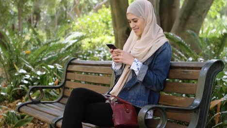 Animación-De-Una-Mujer-Asiática-Sonriente-Con-Hijab-Usando-Un-Teléfono-Inteligente-Sobre-El-Parque