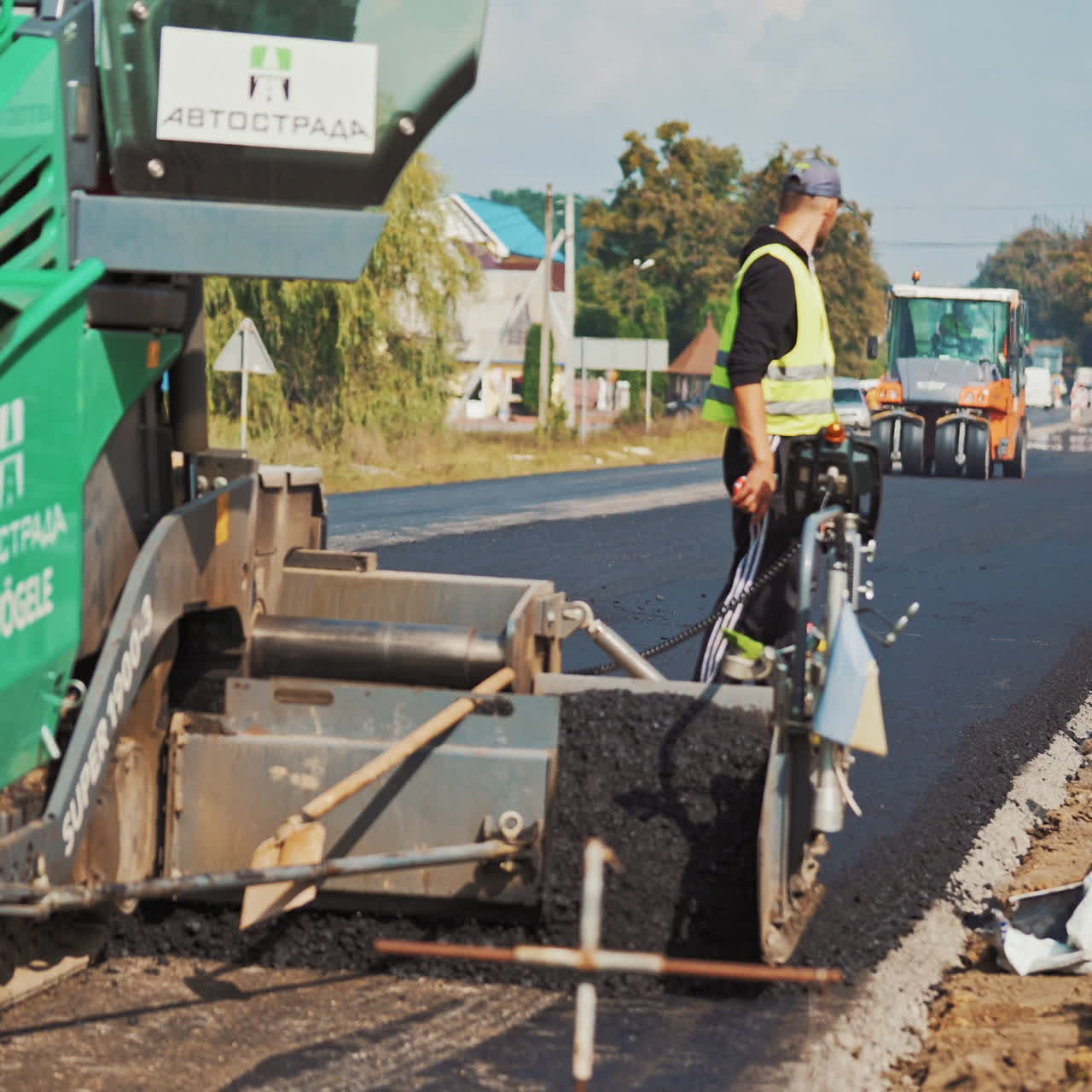 Asphalt machine lays asphalt on highway on the background of heavy machinery at day. Workers in protective uniform control the work of asphalt paver machine during road construction.