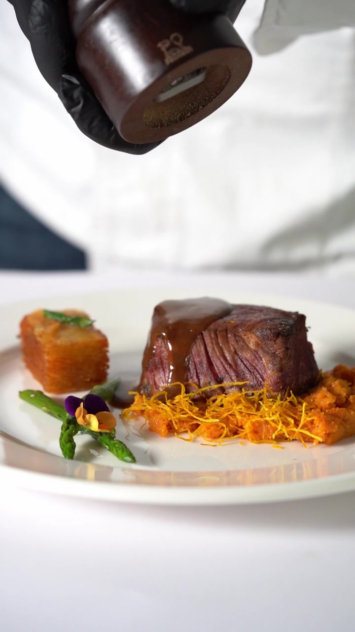 A chief plating Juicy grilled beef steak served on creamy mashed vegetables in a minimalist plate, close up shot, insert shot