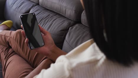 Mid-section-of-gender-fluid-male-having-a-video-call-on-smartphone-while-sitting-on-the-couch-at-hom