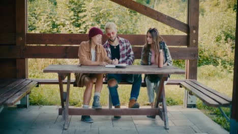 Woman-Writing-In-Diary-Sitting-Next-To-Friends-On-Bench