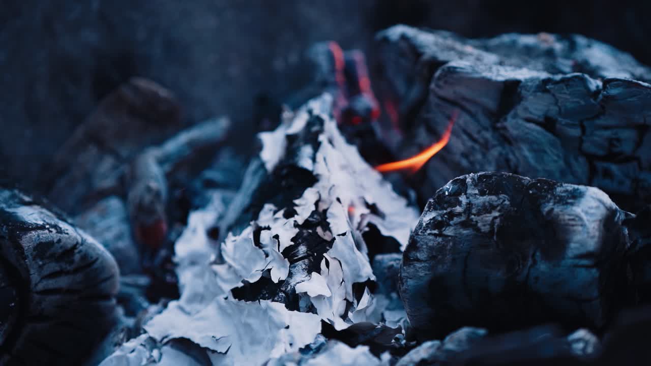 Dark smoldering logs after burned fire. Firewood and embers burning slightly. Close-up. Slow motion.