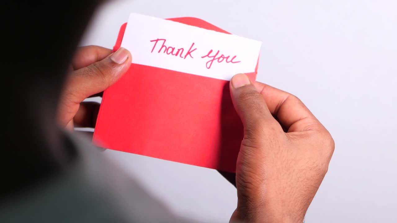 persona sosteniendo un sobre rojo con una nota de agradecimiento