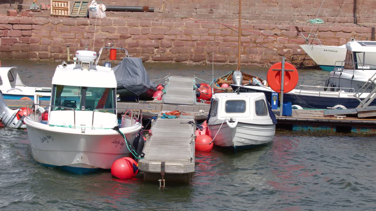 Moored boats sway vigorously at marina pontoon in daylight, rough waves, overcast natural lighting