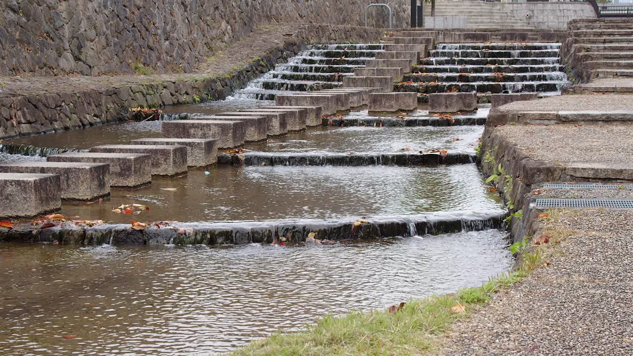 Water trickles down shallow stone steps in narrow city park canal