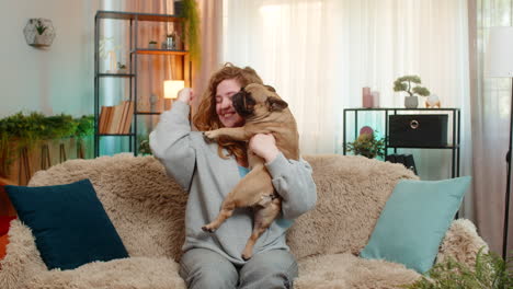 young woman lifts pug dog with joy on sofa celebrating success and sharing happy cheerful emotion