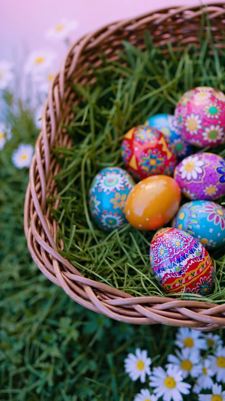 Top-down view of a wicker basket filled with colorful, intricately painted Easter eggs on grass