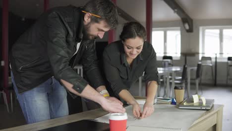 young man and woman working on a project, drawing and thinking in modern office. using compass. coffee cup and laptop on the table. shot in 4k.