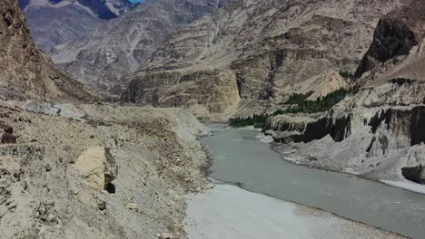 aerial drone flying over a mountain cliff towards the fast flowing gray indus river in skardu pakistan overlooking the large mountains during a sunny summer day