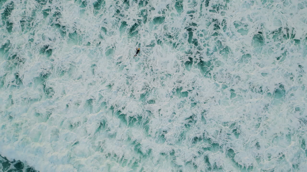Aerial foaming sea water splashing rolling in slow motion. Surfer swimming ocean