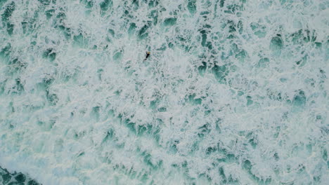 aerial foaming sea water splashing rolling in slow motion. surfer swimming ocean