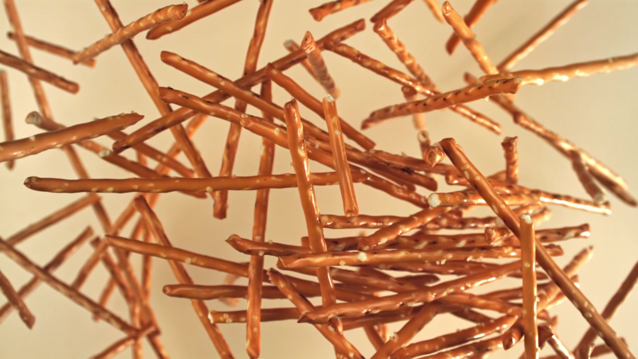 Bastoncini di pretzel dorati sospesi in aria su uno sfondo chiaro.
