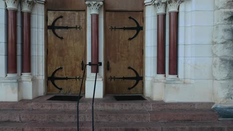 Dolly-push-in-to-old-school-antique-wooden-doors-with-black-bracing-hardware-outside-chapel