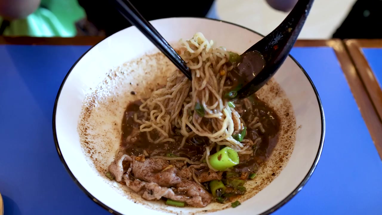 Ripresa dall'alto di mani che usano bacchette e un cucchiaio nero per mangiare noodles tailandesi.