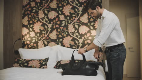 Sexy-businessman-putting-travel-bag-on-bed.-Successful-man-unpacking-luggage