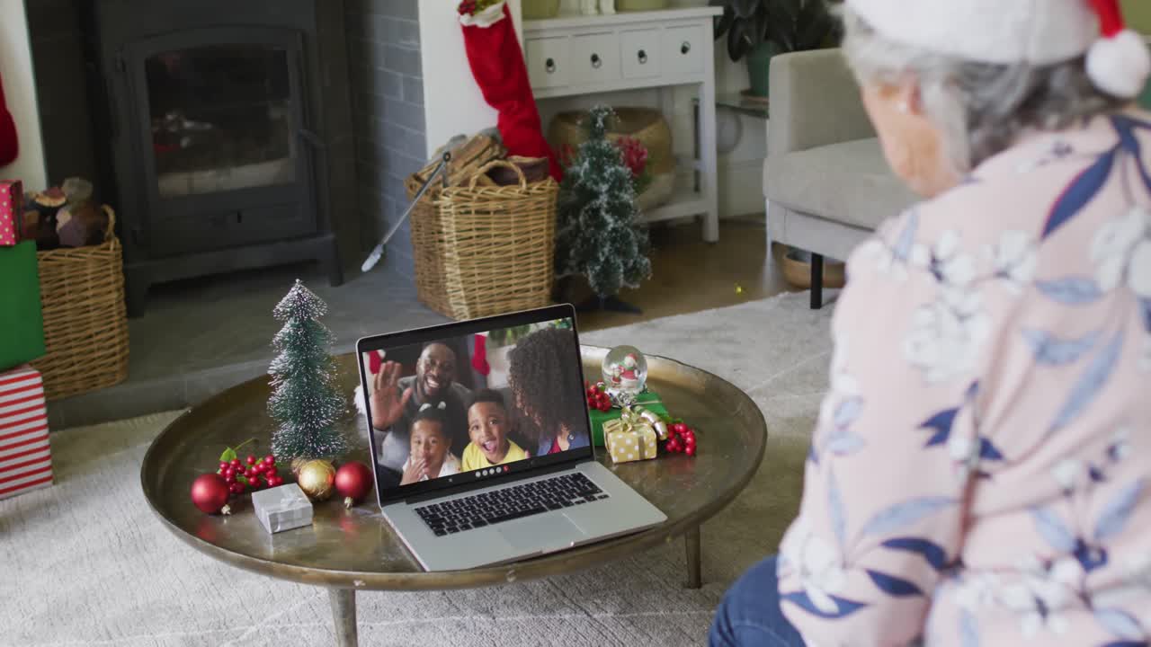 mujer caucásica mayor usando una computadora portátil para una videollamada de navidad con una familia sonriente en la pantalla