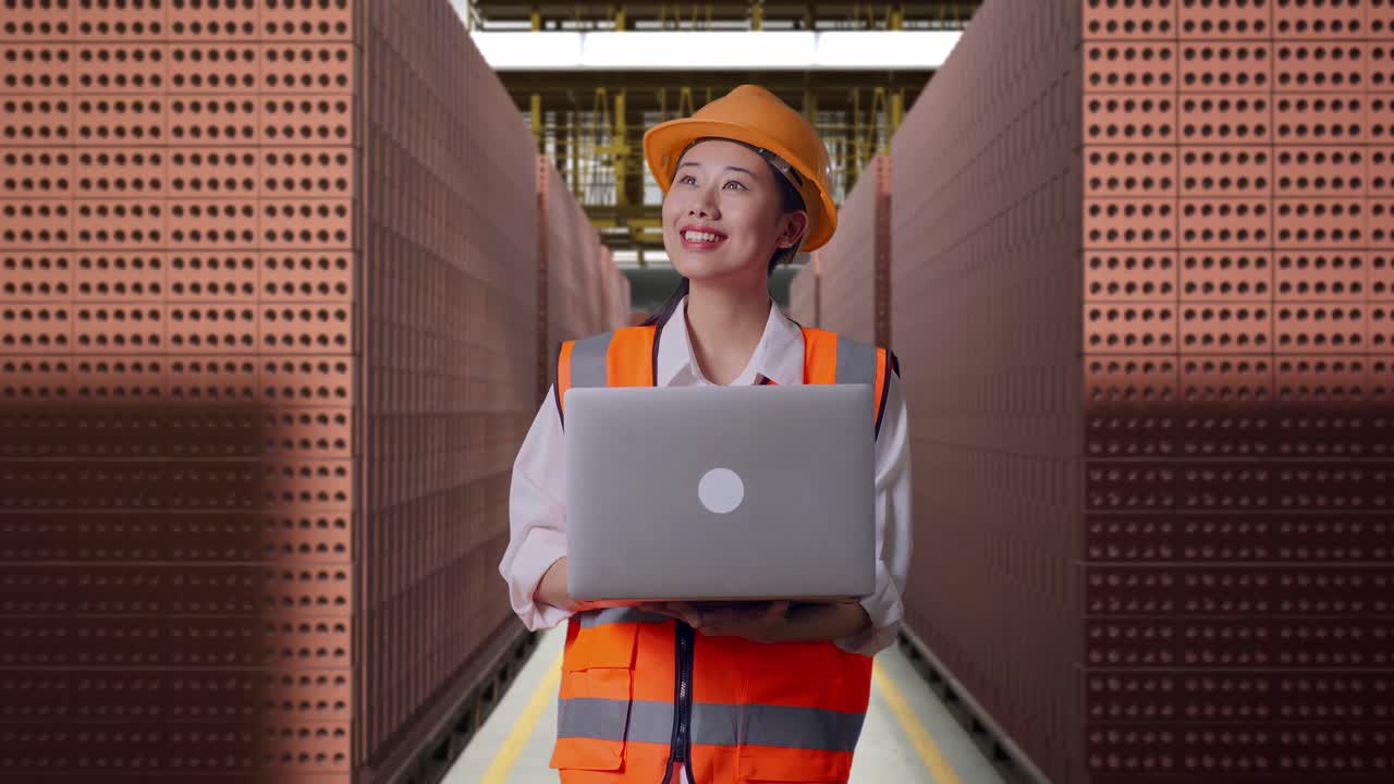 Asian Female Engineer With Safety Helmet Working On A Laptop And Looking Around While Standing With Red Brick Packed in Stacks Are Stored