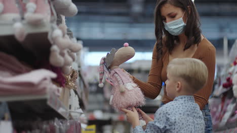 A-woman-in-a-mask-with-a-boy-choose-toys-in-a-super-market