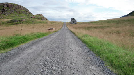 aerial low angle forwarding shot of a one way gravel road with a lonely house on a field of grass