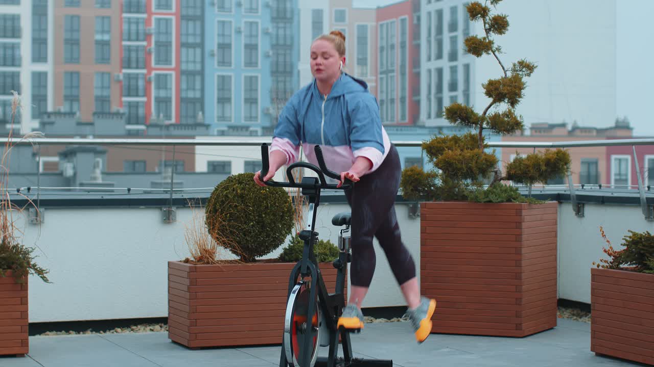 건강한 백인 여성이 집 옥상 체육관에서 정지 자전거 기계 자전거에서 운동을 하고 있습니다.