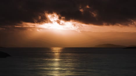 as the sun sets, the tranquil waters reflect the warm orange and red hues of the sky and distant islands.