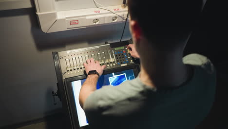 person adjusting controls on a digital panel with hand, manipulating sliders and buttons, working in a professional studio setting, interacting with equipment while focusing on screen