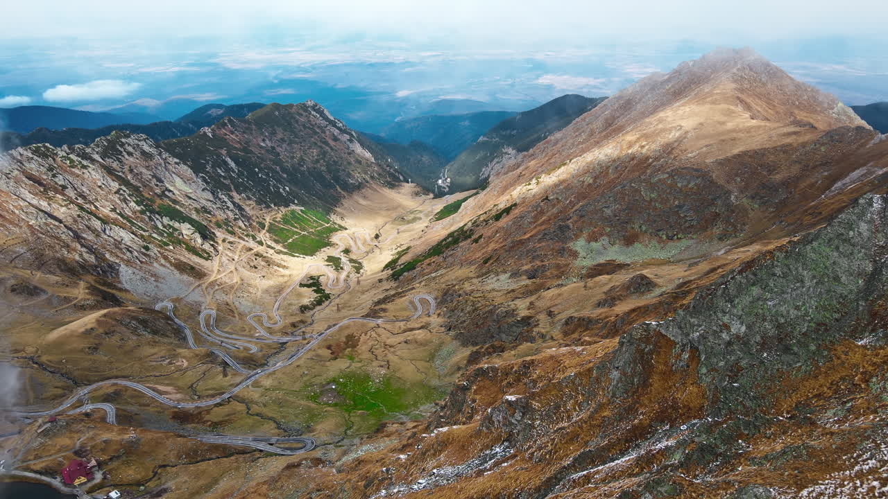 Aerial drone view of nature in Romania. Transfagarasan route in Carpathian mountains, snow on mountains rocky slopes, valley, clouds