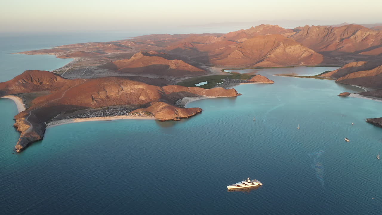balandra 해변의 영화 같은 드론 샷, 붉은 언덕, 청록색 바다, 백사장 해변 및 산의 전망, 만에 보트가 있는 넓은 회전 공중