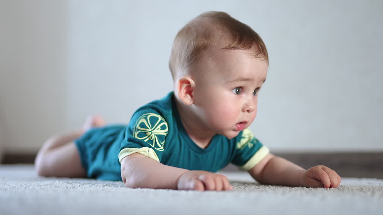 Caucasian baby lying on the floor saliva dripping from his chin. Cute child lowers his head and opens mouth. Close up.