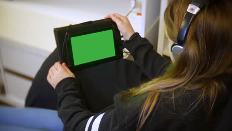 el primer plano de una joven se sienta en casa usando su tableta con sus auriculares puestos