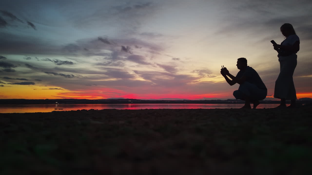 Silhouettes of people with cell phones at sunset on a beach