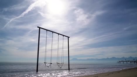footage of swings in a beach in water or the sea in portugal while the water or the sea is moving beneath them and nights and evening sky is visible with clouds in 4k resolution. a pier in the back.