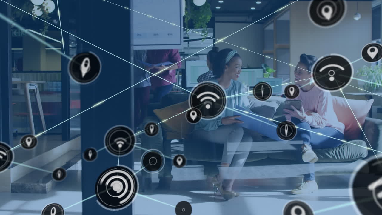 Animation of network of digital icons against two diverse women discussing at office