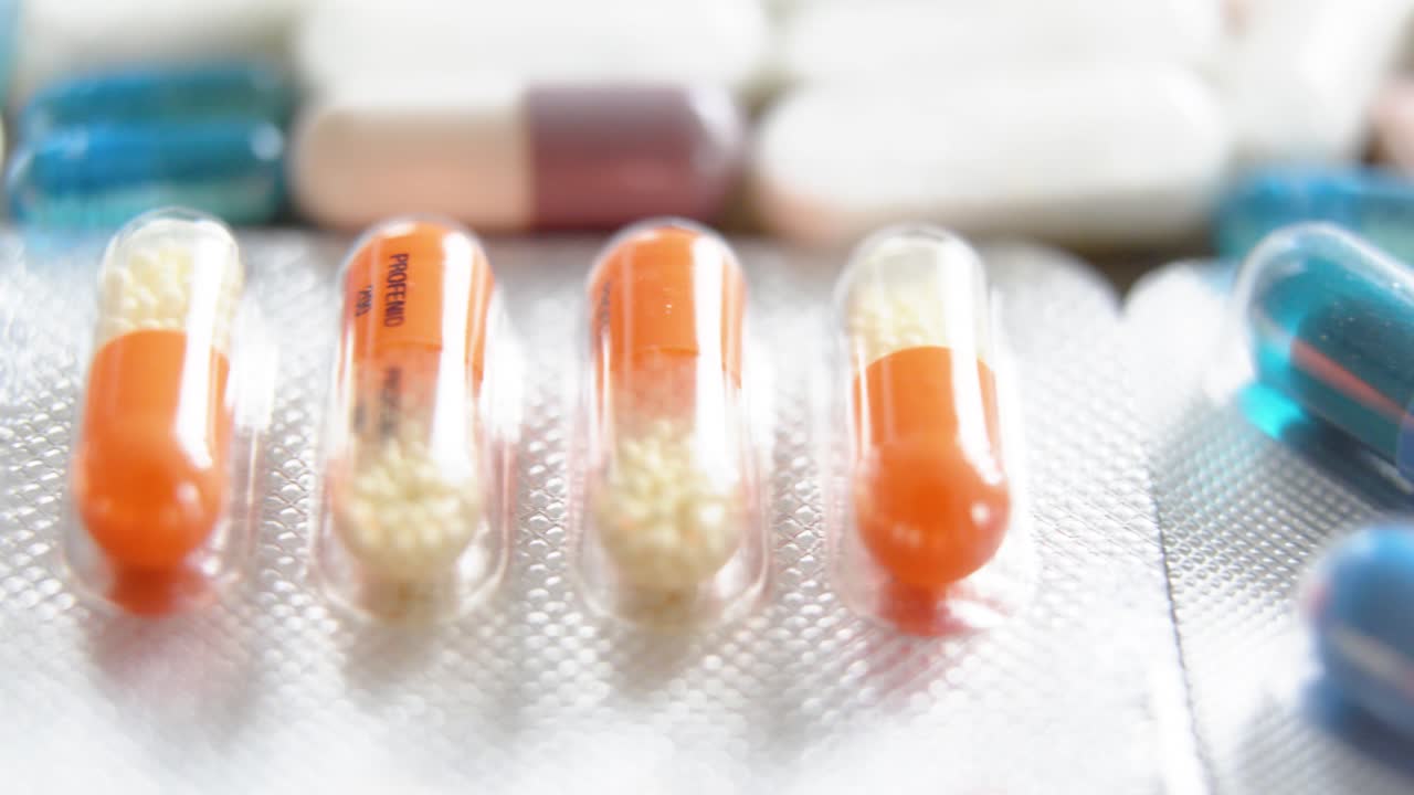close up of transparent blue capsules in blister packaging with other pills in background