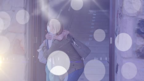 Animation-of-light-spots-over-caucasian-woman-and-her-daughter-wearing-face-embracing