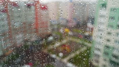 Wet window on blurred city background. Raindrops moving down on glass window at rainy weather. Water droplets on window pane.