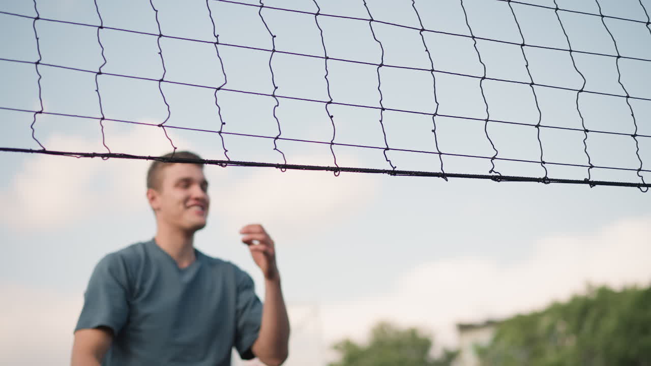 Athlete jumps high and spikes volleyball over net, showing strength and precision, bright sky and sports structures create dynamic sports setting